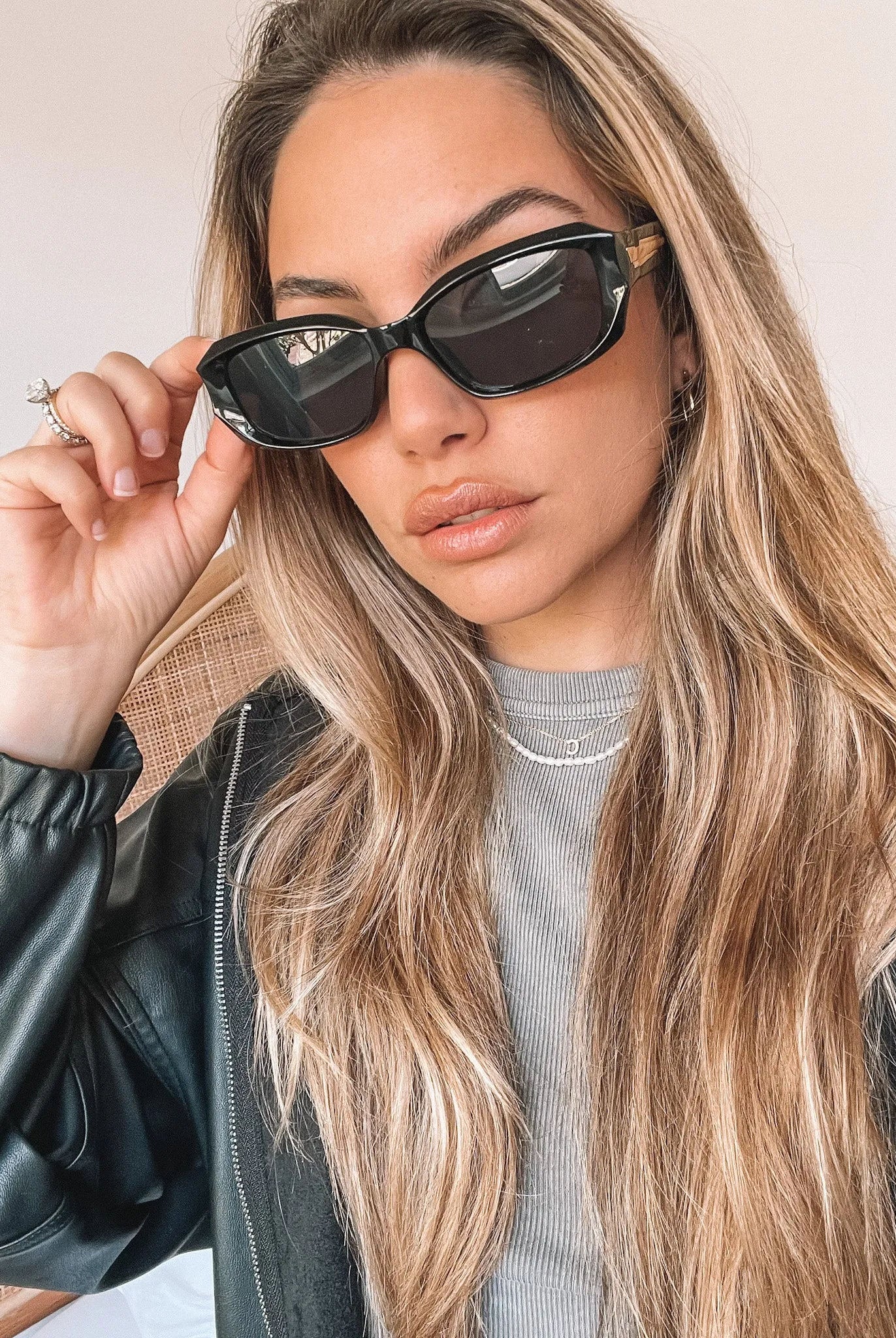 Black rectangular sunglasses with a glossy frame and dark tinted lenses, displayed on a light beige curved surface against a plain white background.