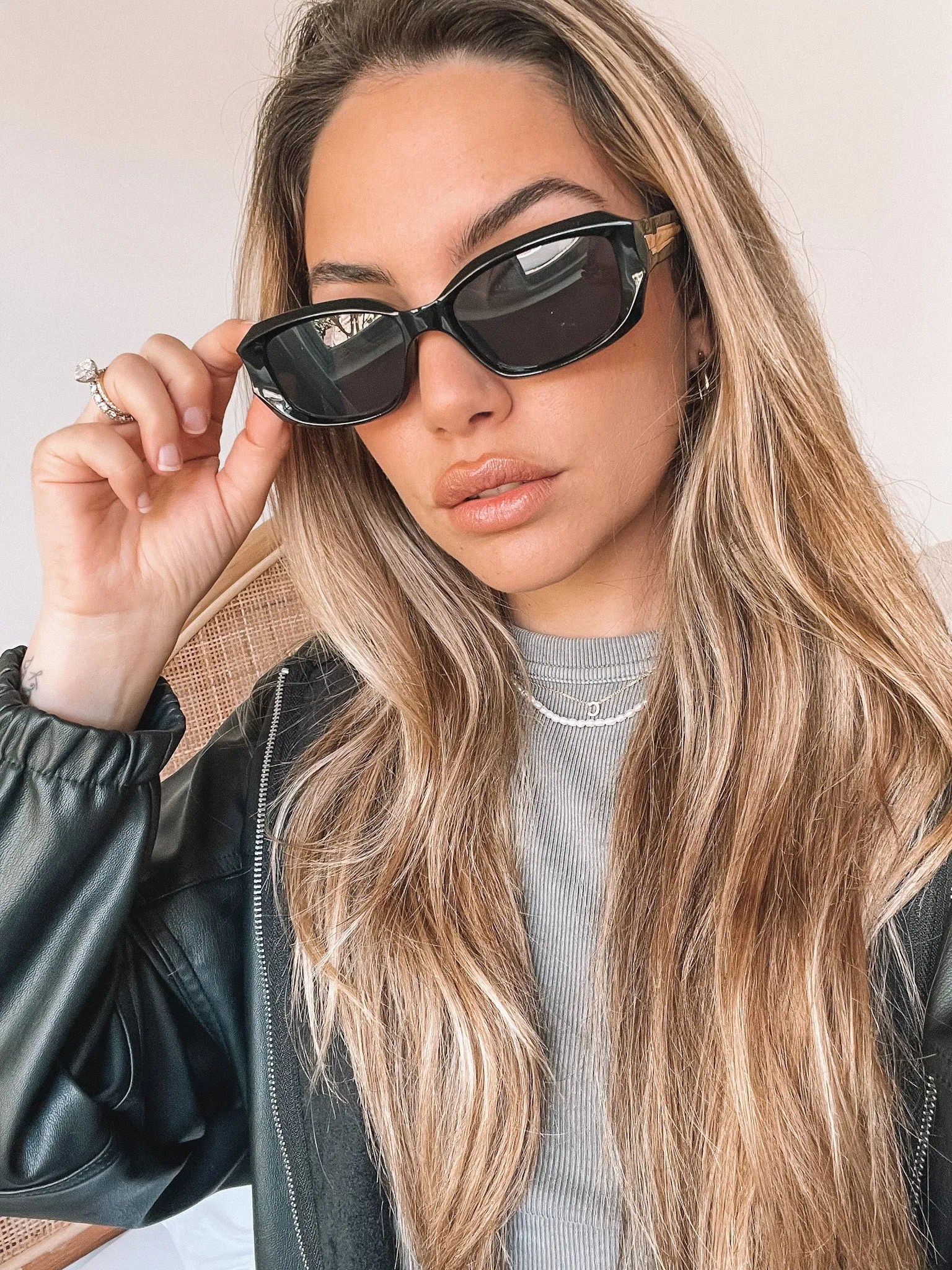 Black rectangular sunglasses with a glossy frame and dark tinted lenses, displayed on a light beige curved surface against a plain white background.