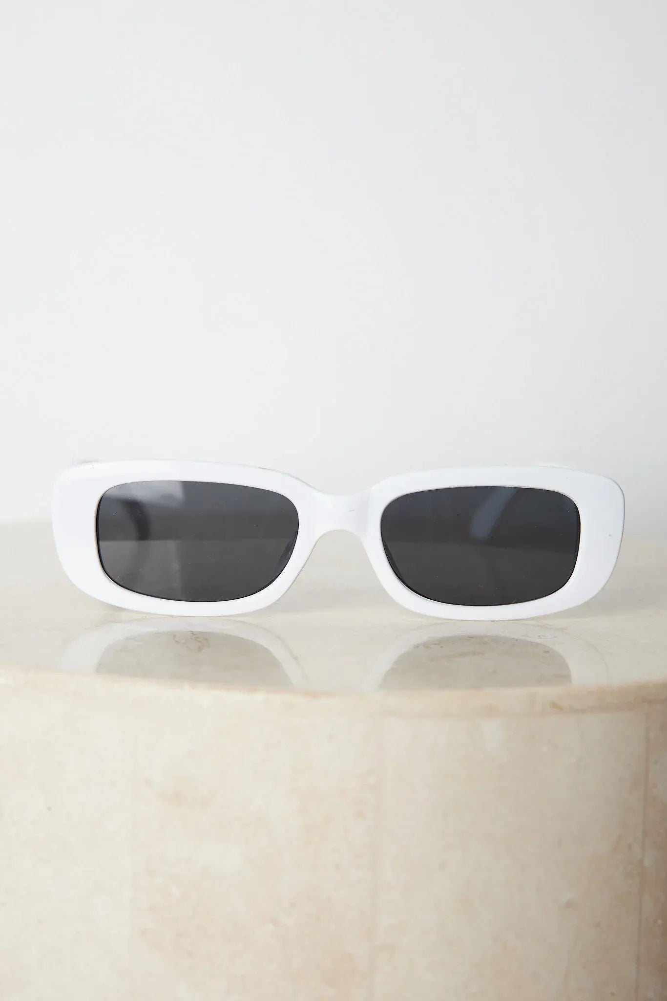 A pair of white-framed sunglasses displayed against a neutral background.