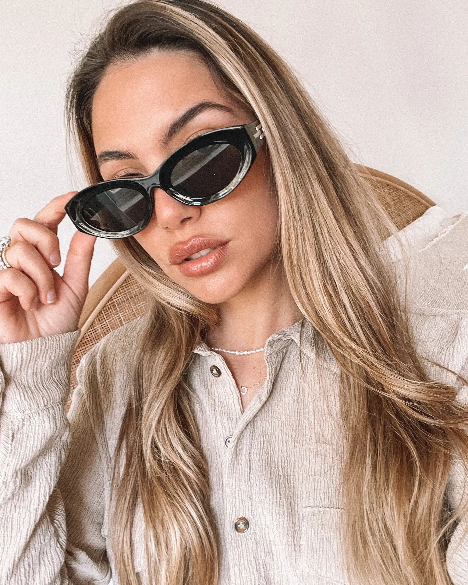 Close-up of a pair of black cat-eye sunglasses with dark lenses, resting on a smooth beige surface against a plain white background.