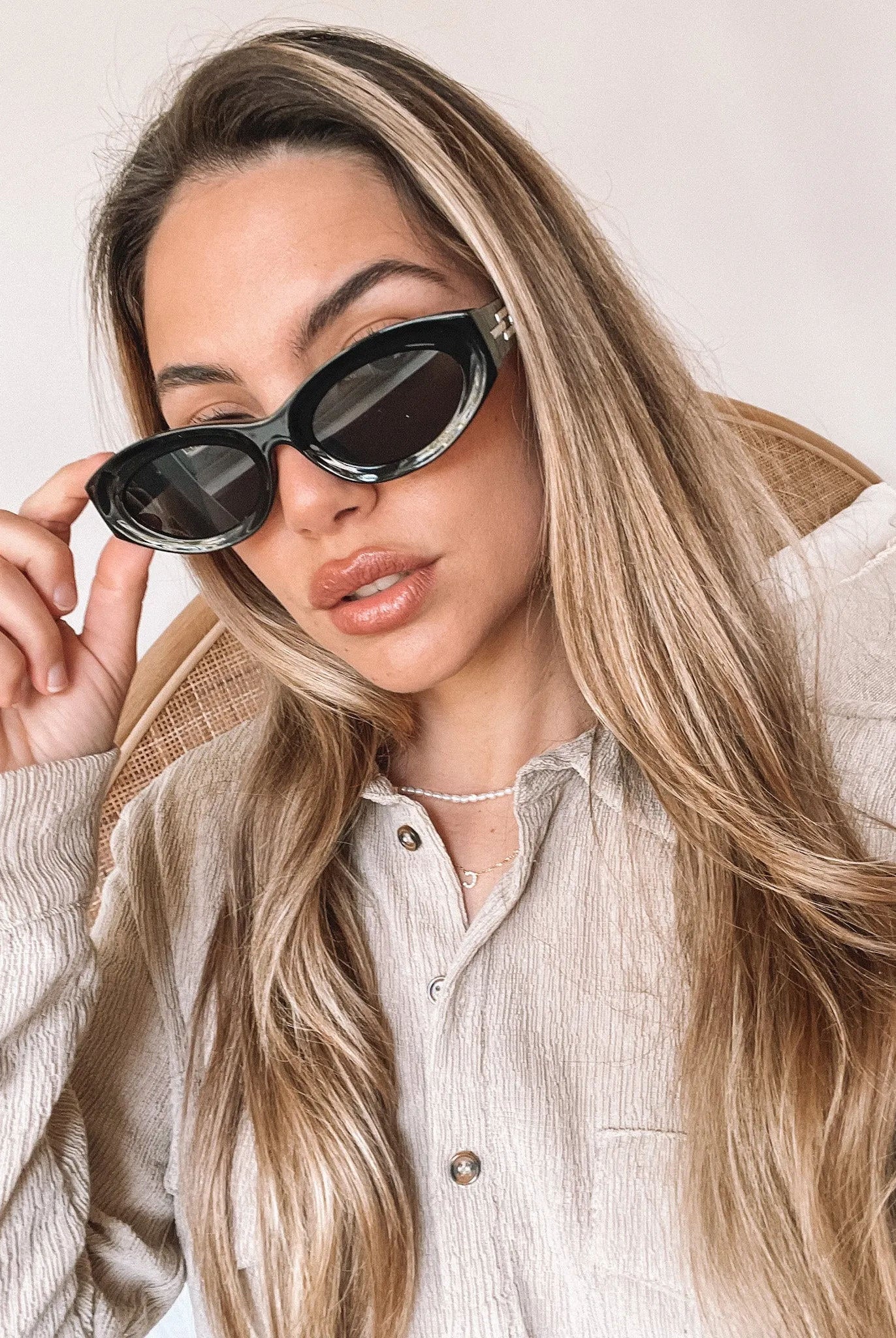 Close-up of a pair of black cat-eye sunglasses with dark lenses, resting on a smooth beige surface against a plain white background.