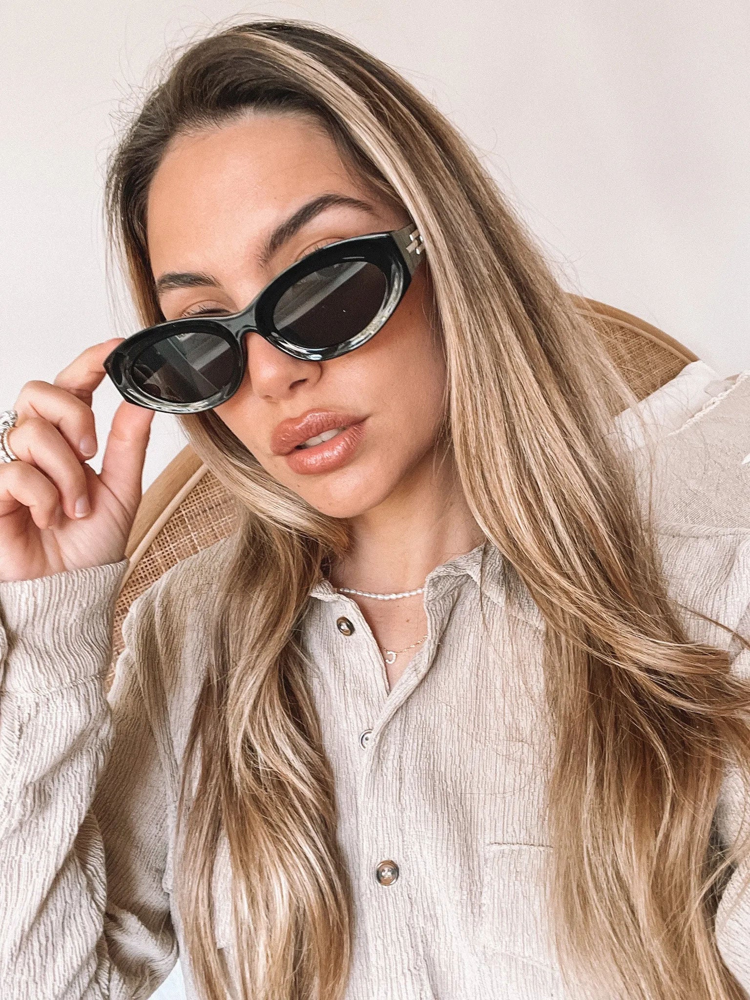 Close-up of a pair of black cat-eye sunglasses with dark lenses, resting on a smooth beige surface against a plain white background.