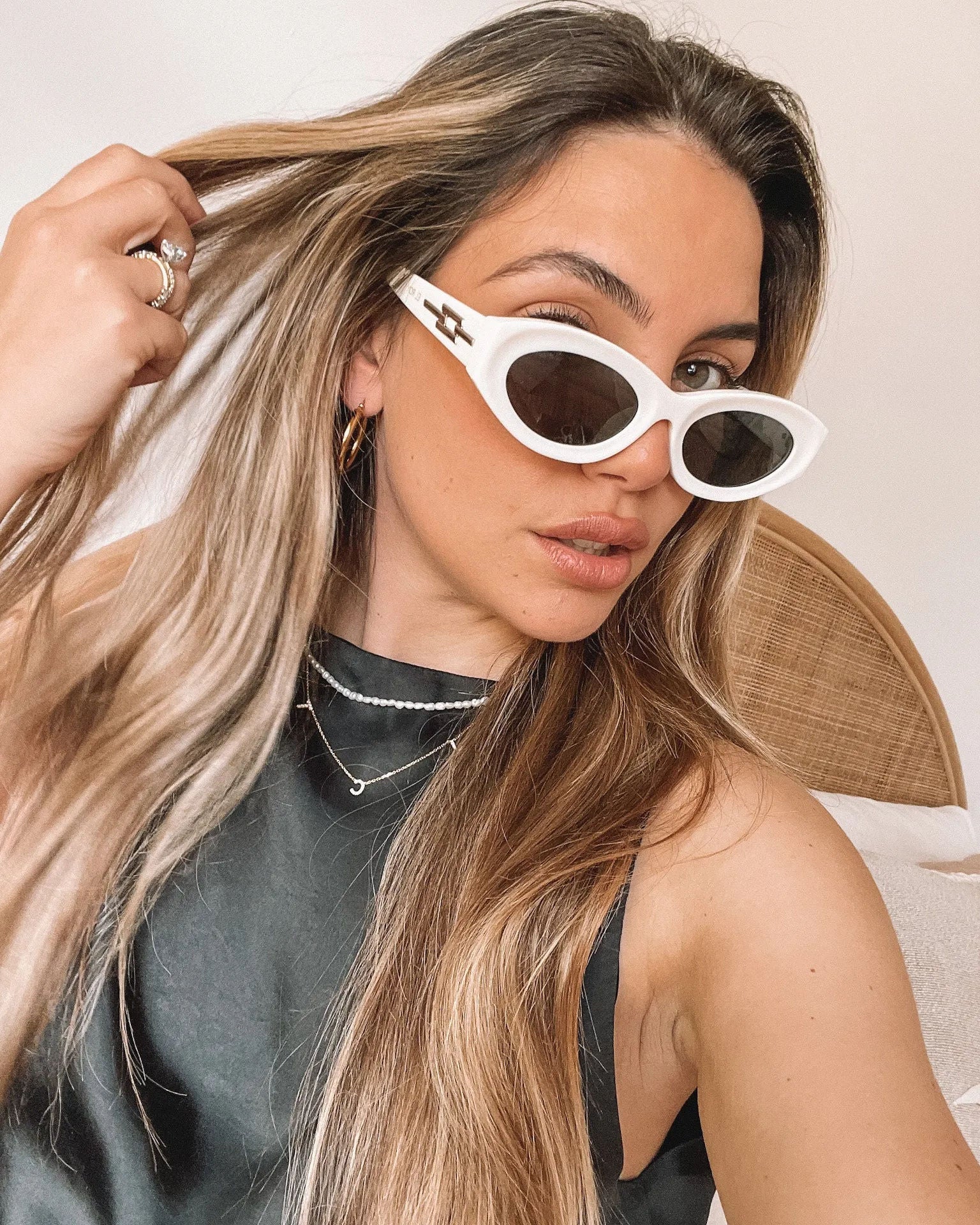 Close-up of a pair of white oval-shaped sunglasses with dark lenses, resting on a smooth beige surface against a plain white background.