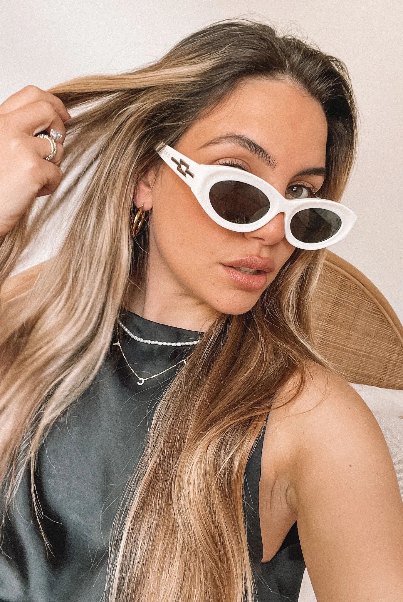 Close-up of a pair of white oval-shaped sunglasses with dark lenses, resting on a smooth beige surface against a plain white background.