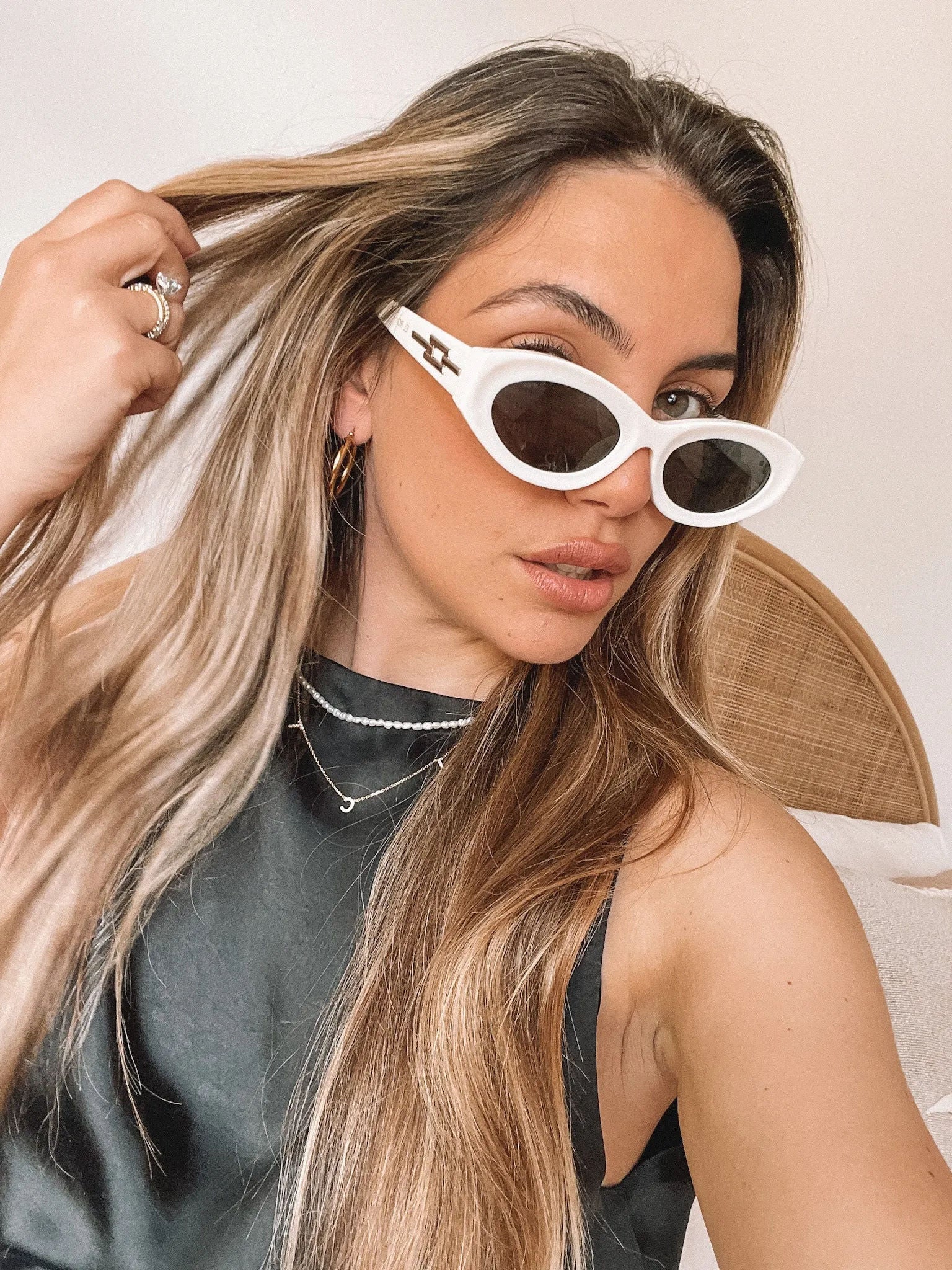 Close-up of a pair of white oval-shaped sunglasses with dark lenses, resting on a smooth beige surface against a plain white background.