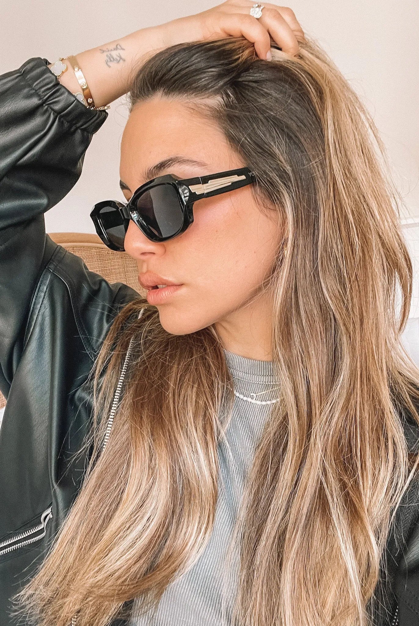Black rectangular sunglasses with a glossy frame and dark tinted lenses, displayed on a light beige curved surface against a plain white background.
