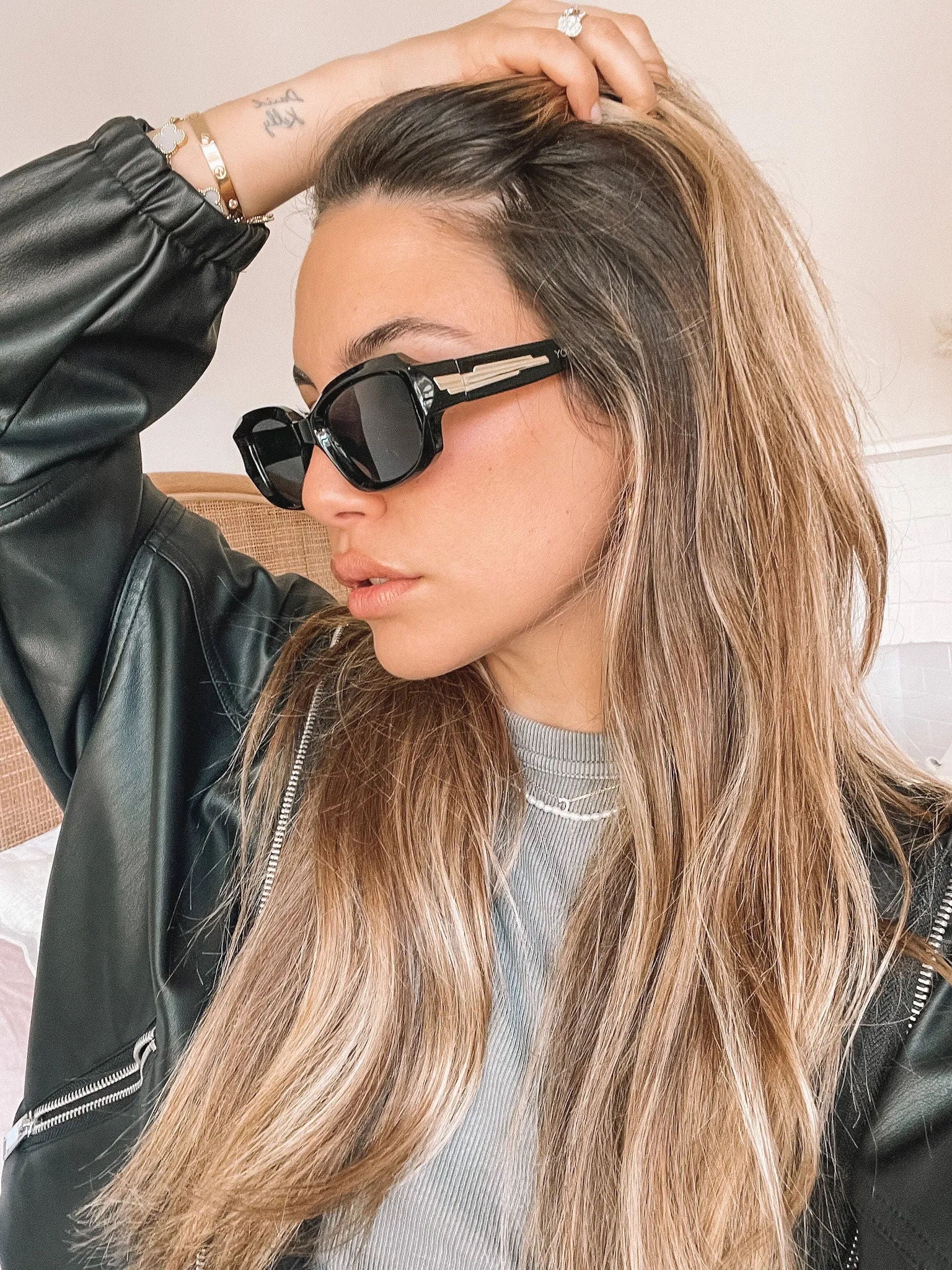 Black rectangular sunglasses with a glossy frame and dark tinted lenses, displayed on a light beige curved surface against a plain white background.
