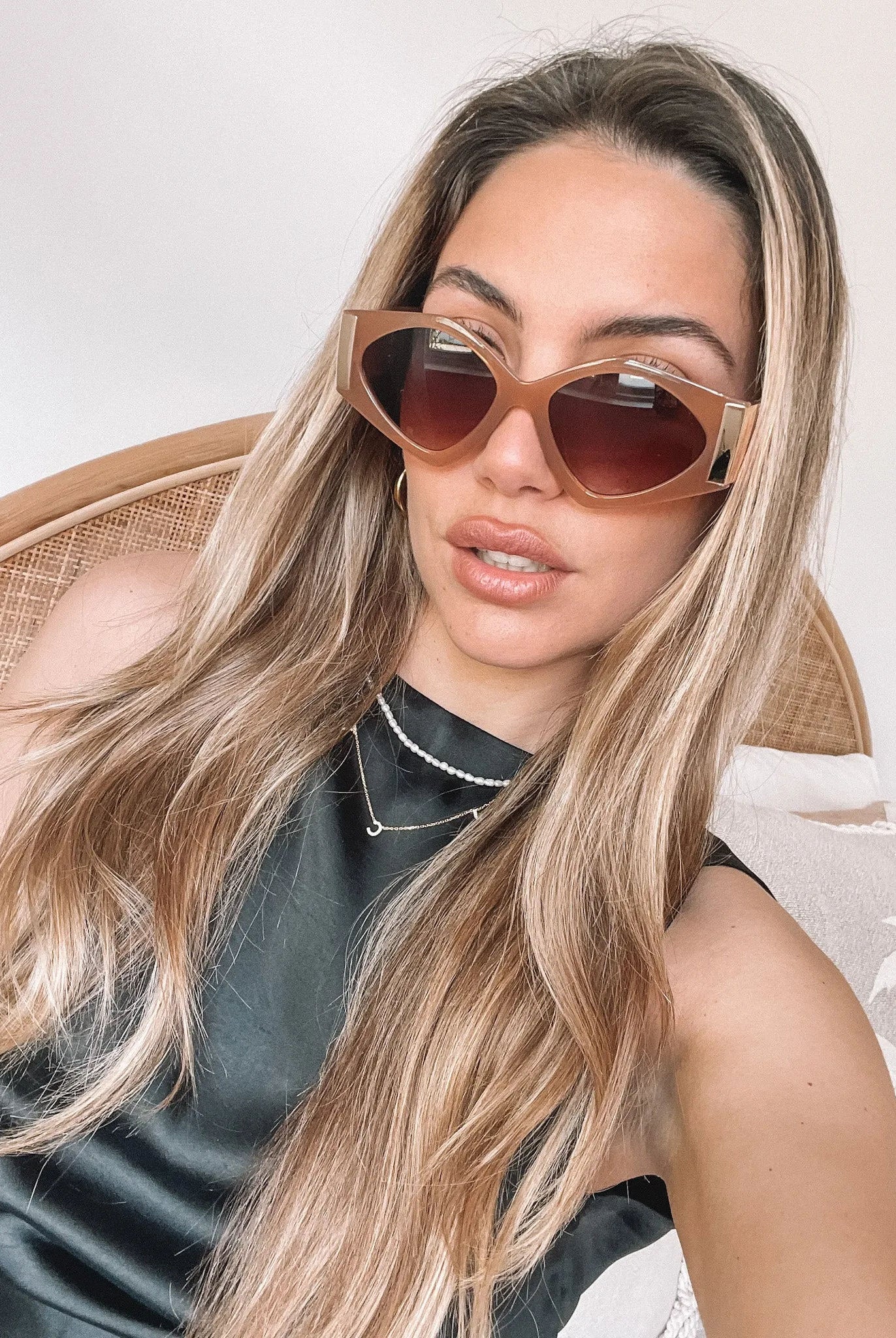 Brown cat-eye sunglasses with thick, glossy frames and dark brown tinted lenses, featuring gold accents on the corners, displayed on a light beige surface against a plain white background.