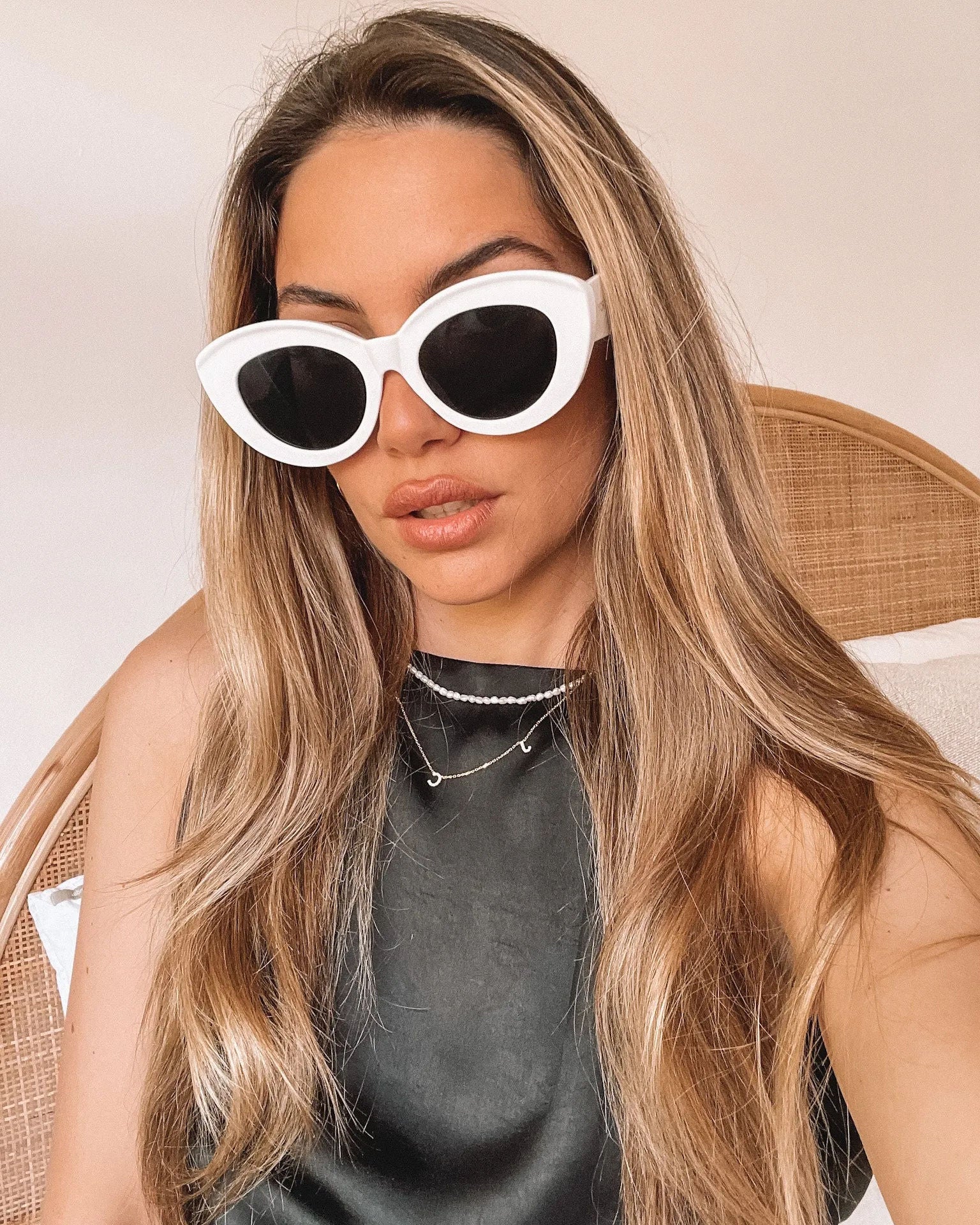 White cat-eye sunglasses with dark lenses displayed on a light beige marble surface against a plain white background.