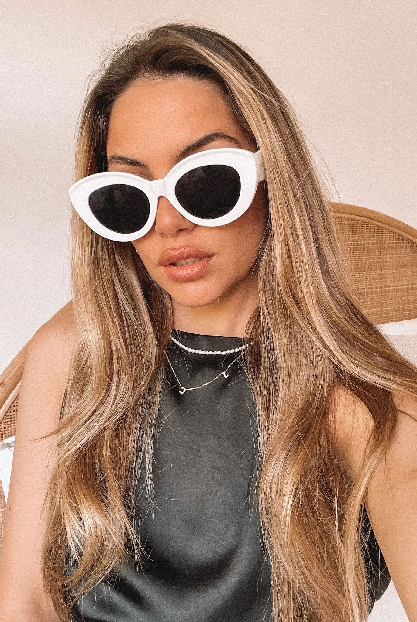 White cat-eye sunglasses with dark lenses displayed on a light beige marble surface against a plain white background.