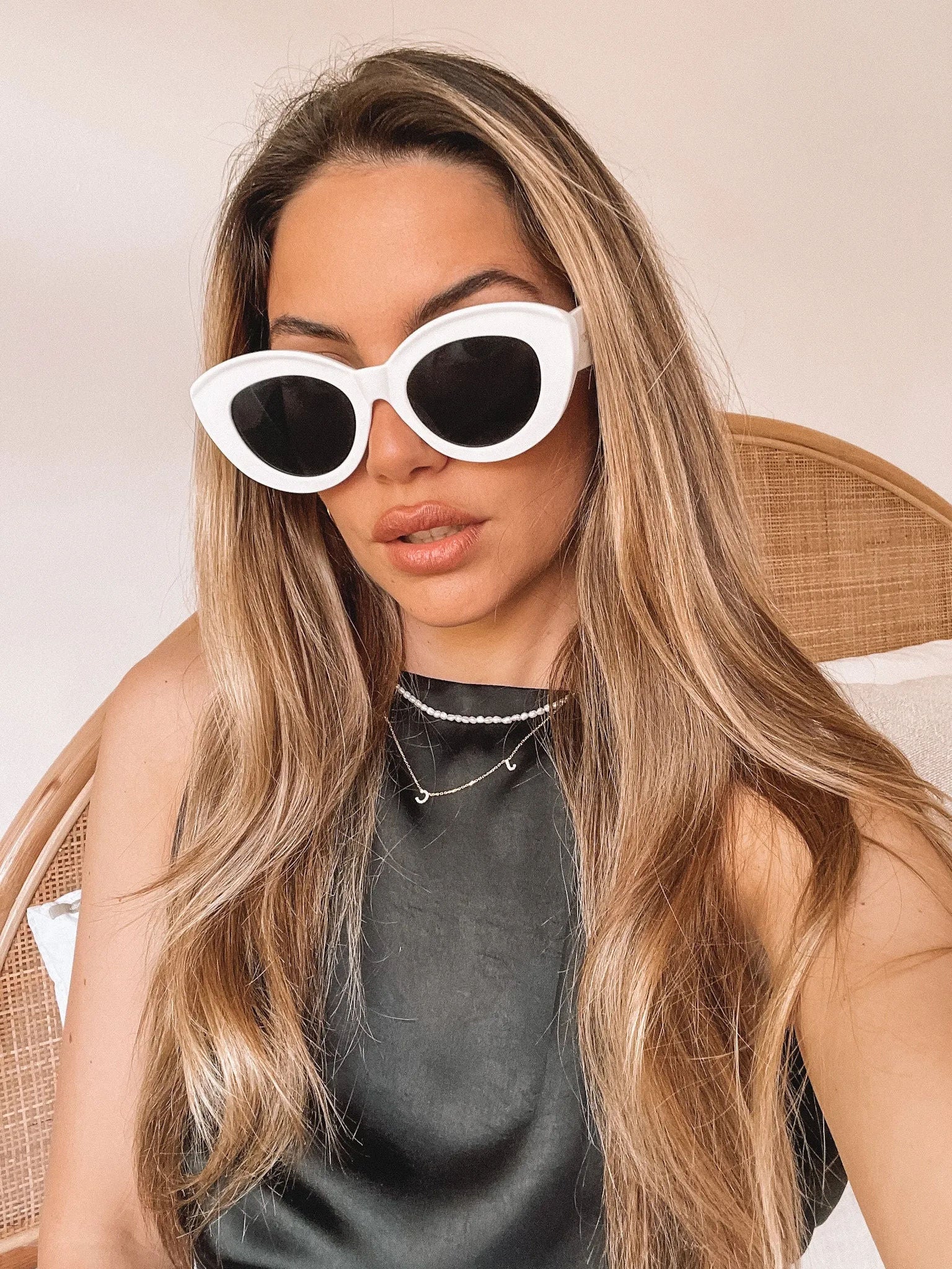 White cat-eye sunglasses with dark lenses displayed on a light beige marble surface against a plain white background.