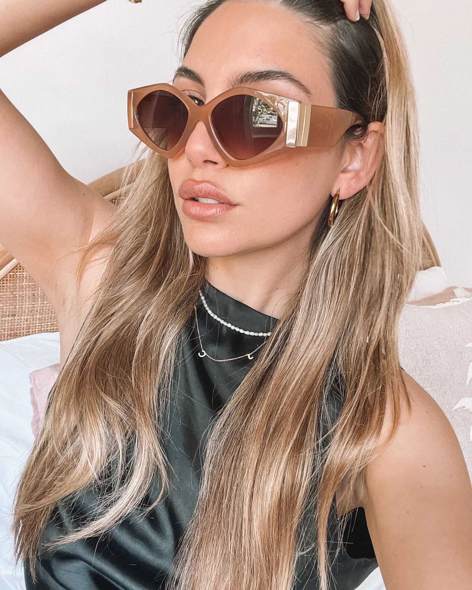 Brown cat-eye sunglasses with thick, glossy frames and dark brown tinted lenses, featuring gold accents on the corners, displayed on a light beige surface against a plain white background.