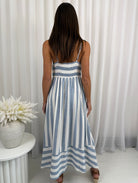 Woman wearing a blue and white striped dress standing in front of white curtains.