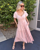Women wearing the Celie Dress in Pink, a relaxed linen midi dress with V-neckline and tiered detail