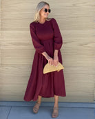 Women wearing the Iolana Dress in Wine Long Sleeve, a cotton midi dress with round neckline and smocked bodice in rich wine