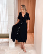 Side view of the Korbela Dress in Black showing the flowing midi length and button-up front detail