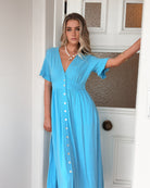 Women wearing the Korbela Dress in Sky Blue, a relaxed linen midi dress with V-neckline and button-up front