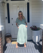 Model wearing the Korbela Sage Midi Dress with sandals and straw bag for a holiday look