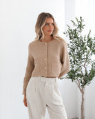 A woman wearing a beige Jacket with long sleeves, round neckline, and center-front buttons. The jacket has a crop length and she is paired with light-colored trousers.