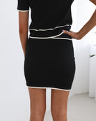 A model wearing a high-waisted, mini-length black knit skirt with white contrasting trim and a matching top.
