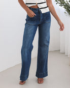 A woman standing in a room with light decor, wearing a striped top and mid-blue Yzabel Jeans with a high waist fit and wide leg silhouette.