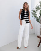 A female model wearing white high-waisted jeans with brown contrasting stitches, paired with a striped black and white top.