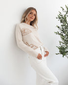 A woman wearing a cream-colored knit top with a round neckline and long sleeves, featuring a print of various items.
