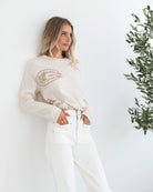 A woman wearing a cream-colored knit top with a round neckline and long sleeves, featuring a print of various items.
