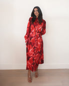 Woman wearing a red floral dress against a white wall