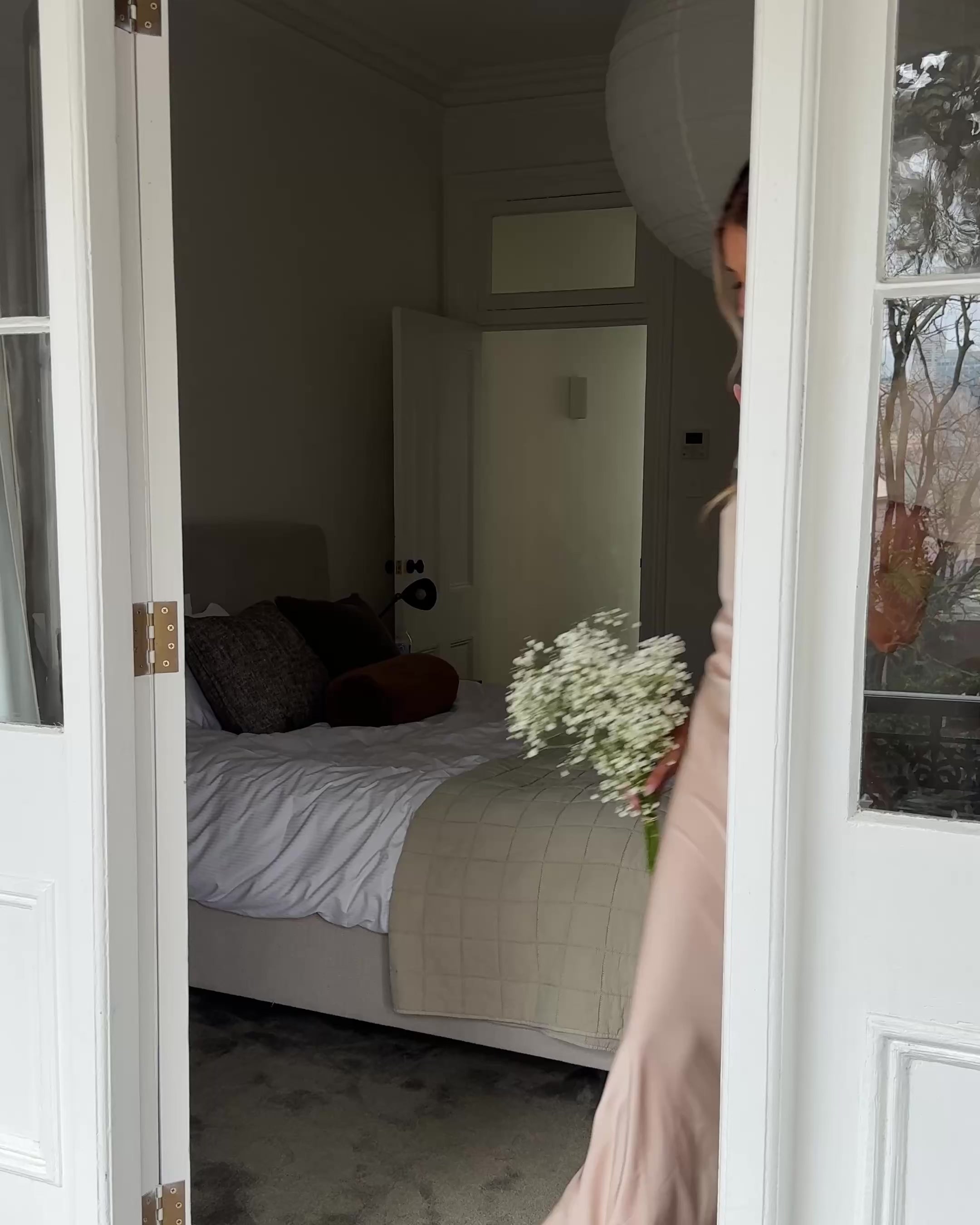 Graceful woman in a beige dress holding a bouquet, suited for wedding celebrations, high-society gatherings, charity dinners, luxury banquets, and elegant affairs, standing in a doorway.