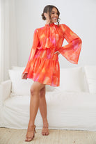Women wearing the Daenerys Mini Dress in Orange Print with bold red and purple print on orange base and long sleeves