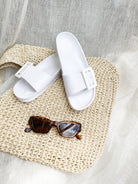 A pair of black summer slides with thick straps, displayed on a flat surface with a knitted texture in the background.