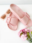 A pair of black summer slides with thick straps, displayed on a flat surface with a knitted texture in the background.