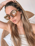 A pair of sunglasses with olive green frames and pink lenses displayed on a surface.