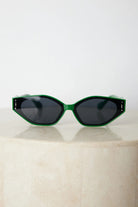 Green geometric-shaped sunglasses with dark lenses resting on a light marble surface against a plain white background.