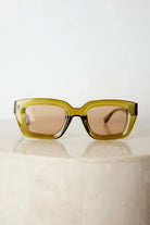 A pair of sunglasses with olive green frames and pink lenses displayed on a surface.