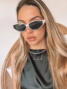 White geometric-shaped sunglasses with dark lenses resting on a light marble surface against a plain white background.