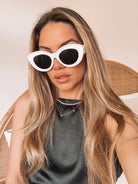 White cat-eye sunglasses with dark lenses displayed on a light beige marble surface against a plain white background.