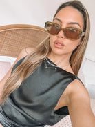 Rectangular sunglasses with translucent olive green frames and brown tinted lenses, displayed on a light beige stone surface against a plain white background.