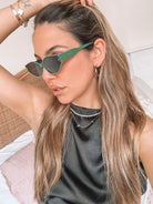 Green geometric-shaped sunglasses with dark lenses resting on a light marble surface against a plain white background.